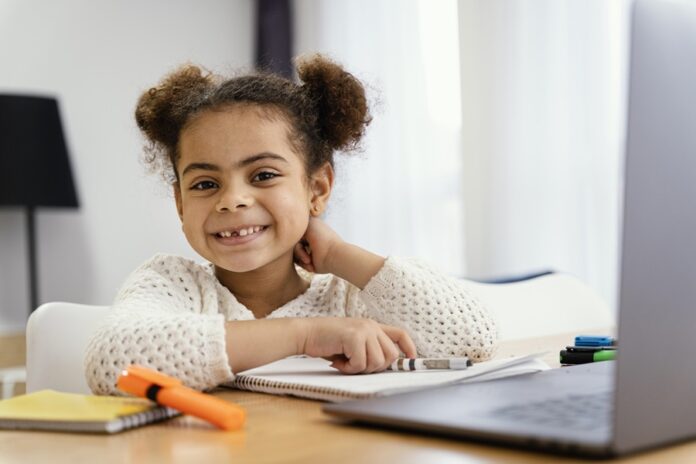 front-view-smiley-little-girl-home-online-school-with-laptopSS